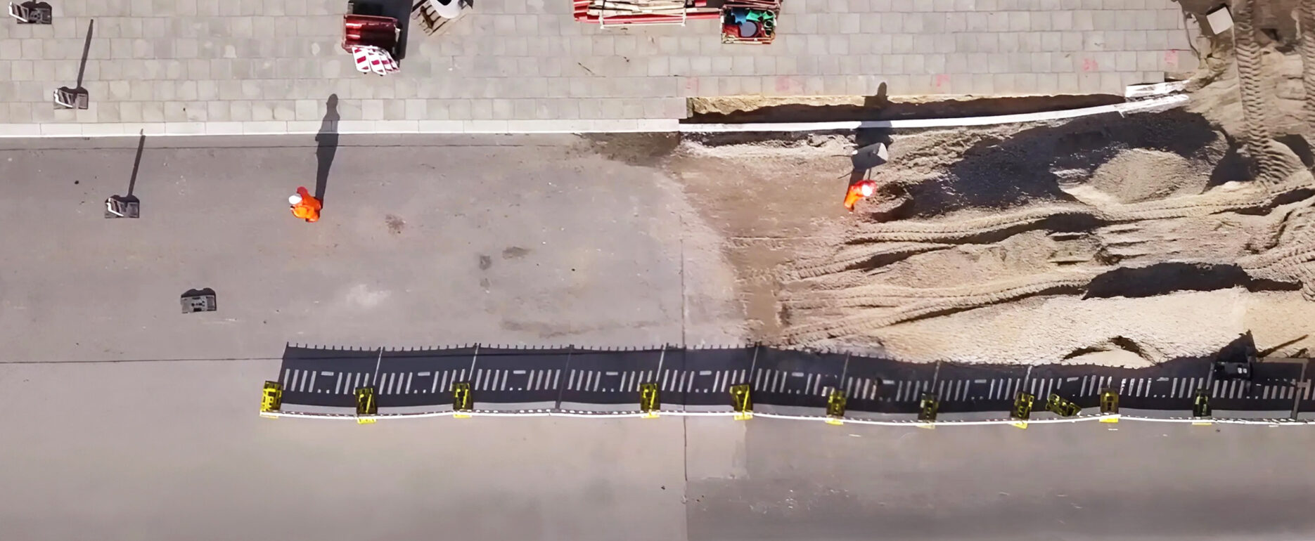 Luftaufnahme einer Baustelle mit Absperrung und zwei Bauarbeitern in Warnkleidung.