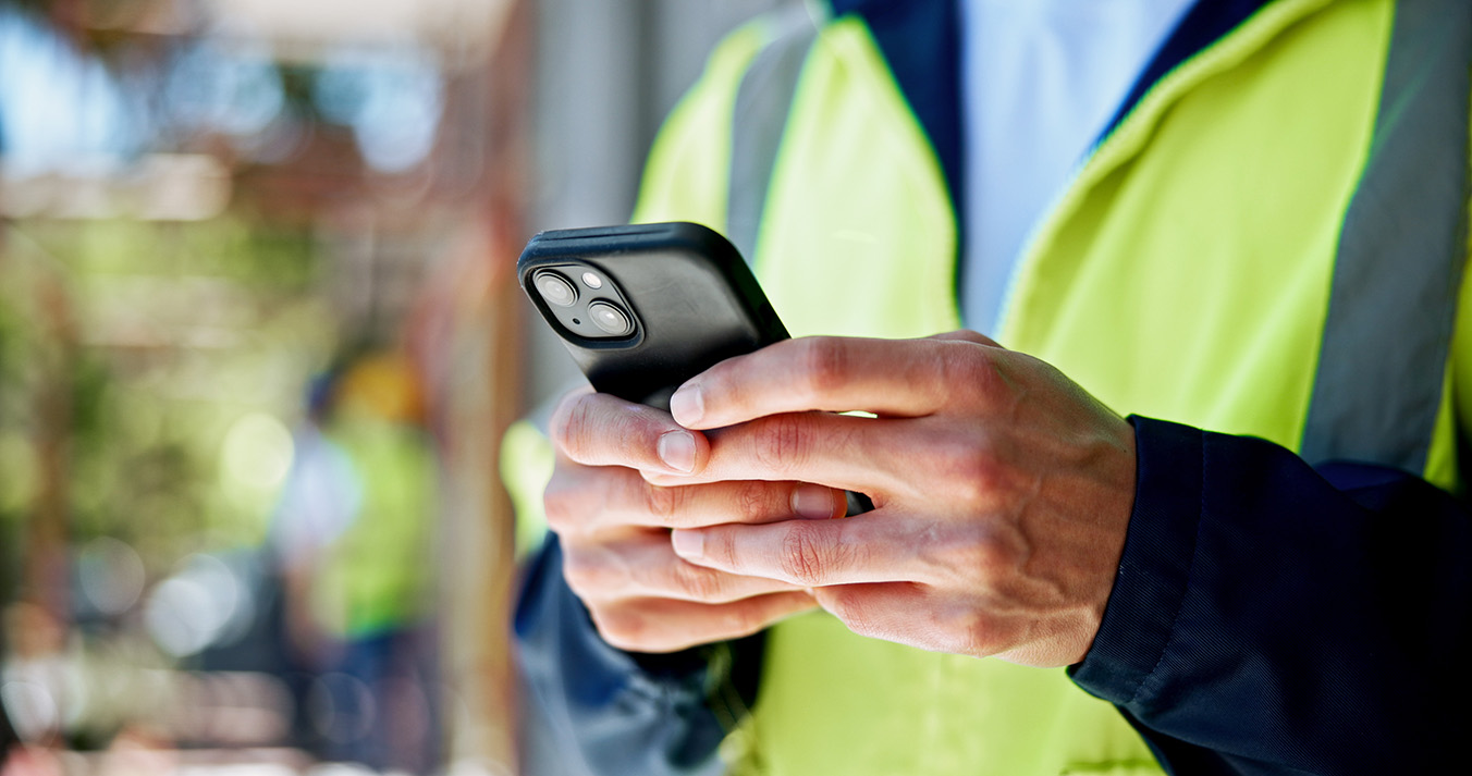 Person in Warnweste hält ein Smartphone.